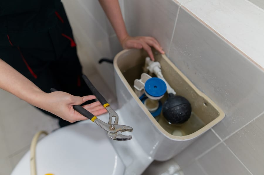 Plumber repairing toilet with an open tank.