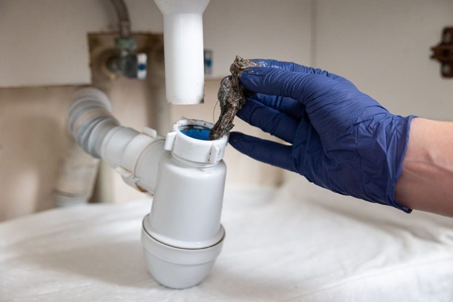 Debris being pulled out of a drain by a gloved hand.