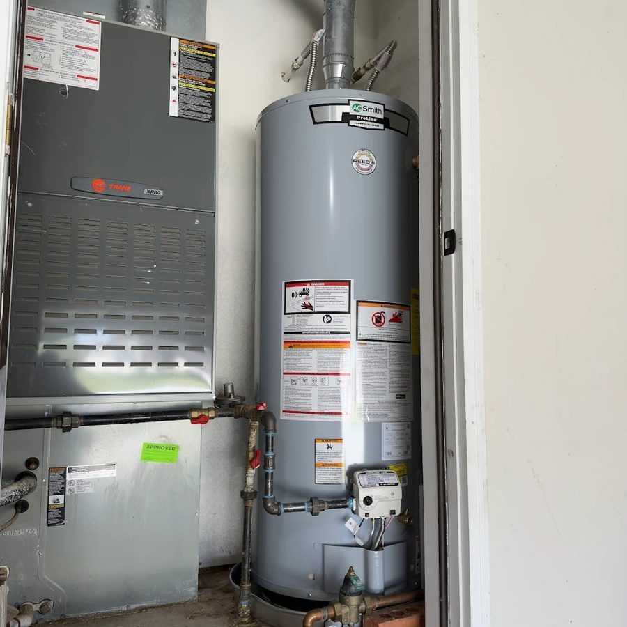Tall gray water heater with label 'A O Smith' beside a furnace in a utility room, with pipes and a valve visible at the base.