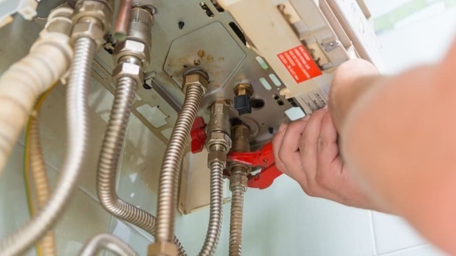 Technician's hand turning a red lever on a metal control panel with braided hoses beneath an industrial machine.