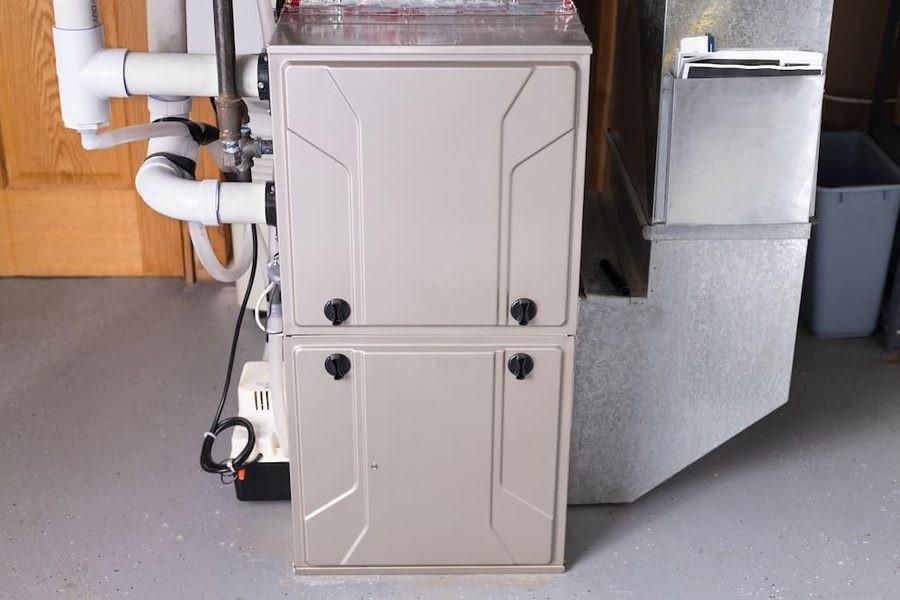 Two-section beige furnace in a basement utility area with PVC piping and metal ductwork visible behind it.